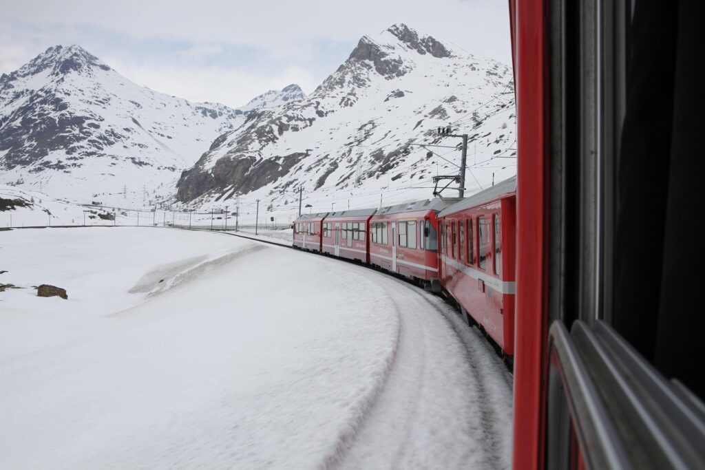 Bernina Express train traveling through snow-covered landscapes in the Swiss Alps.