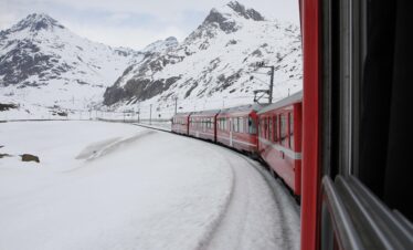 Bernina Express train traveling through snow-covered landscapes in the Swiss Alps.
