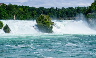 Rhine Falls in Switzerland, with powerful water cascading over the rocks and surrounded by lush greenery.