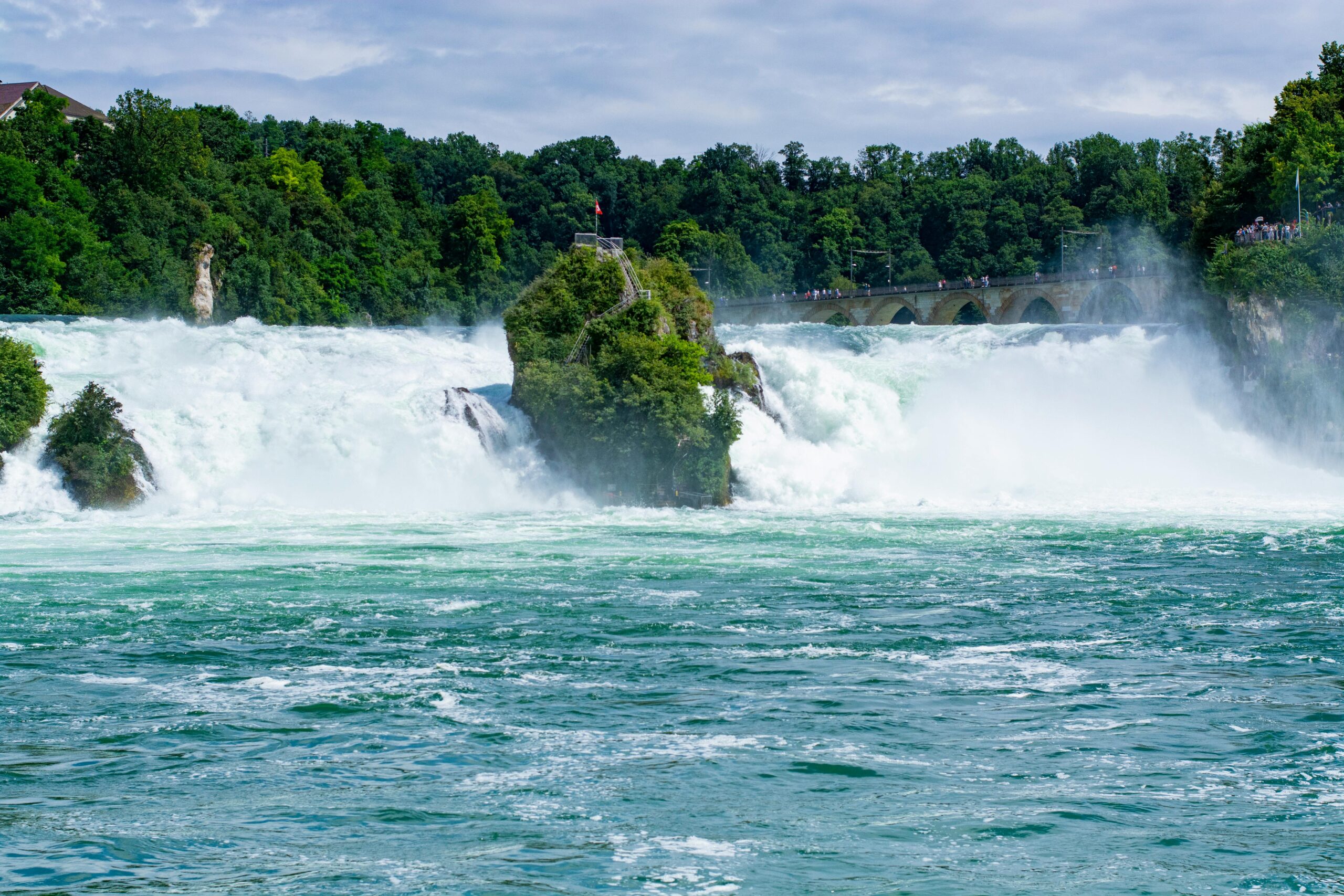 Rhine Falls in Switzerland, with powerful water cascading over the rocks and surrounded by lush greenery.