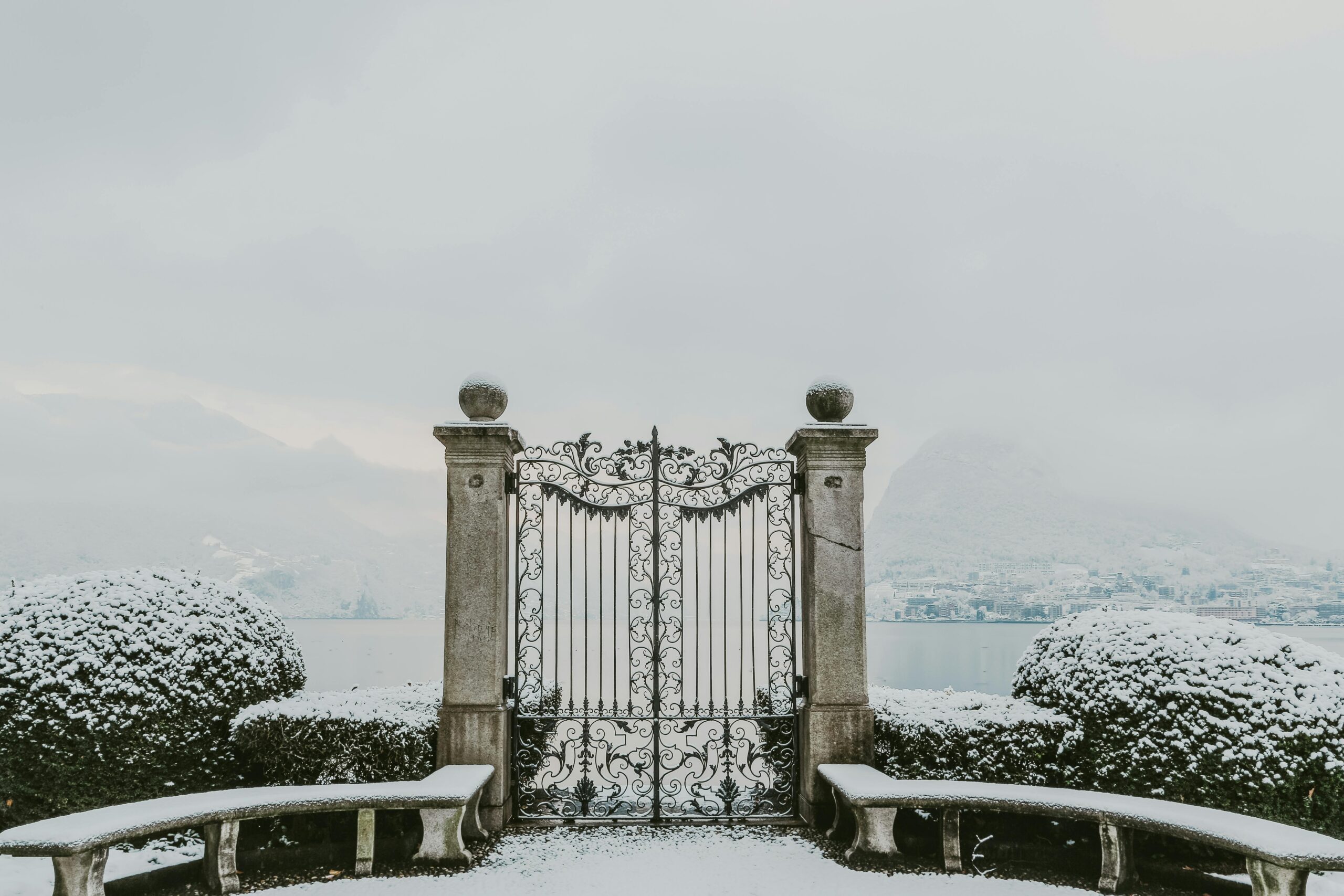 Gate at Parco Ciani, overlooking Lake Lugano with snow-capped mountains in the distance.