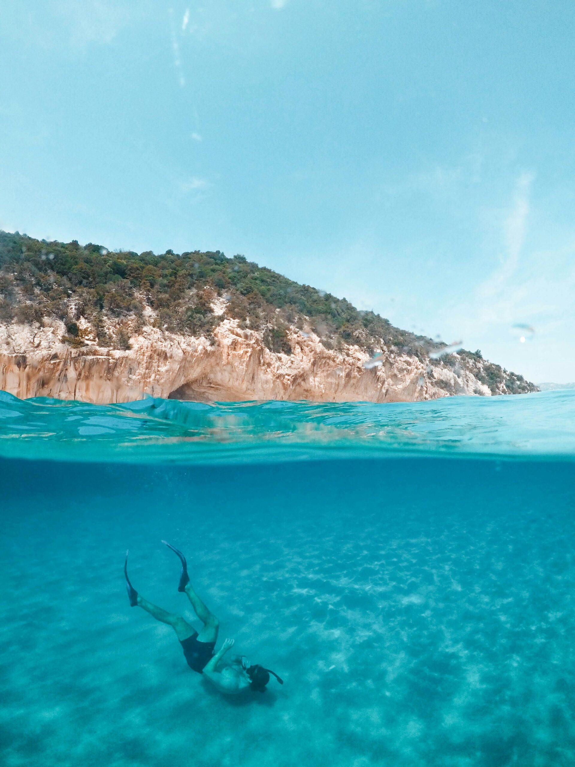Person scuba diving in crystal-clear water with green hills in the background.
