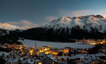 St. Moritz at almost night, with a frozen lake reflecting the fading light and snow-covered mountains in the background.