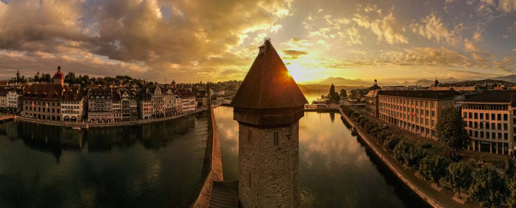 Sunset over Chapel Bridge in Lucerne, with the colorful sky reflecting on the water and the historic wooden bridge in the foreground.