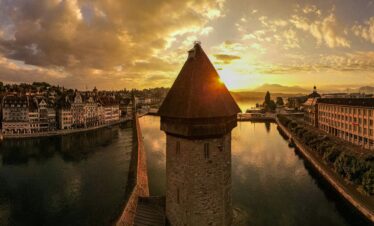 Sunset over Chapel Bridge in Lucerne, with the colorful sky reflecting on the water and the historic wooden bridge in the foreground.