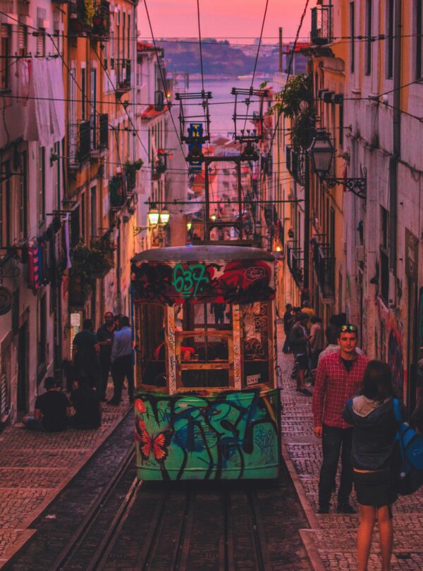 A picturesque view of Lisbon at sunset, with the iconic Elétrico tram winding its way through the streets, bathed in the warm glow of the setting sun.