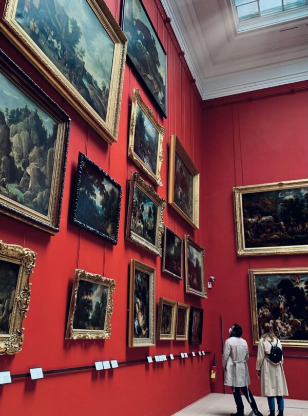 Visitors admiring a painting in a museum, standing in front of a famous artwork while appreciating its details.