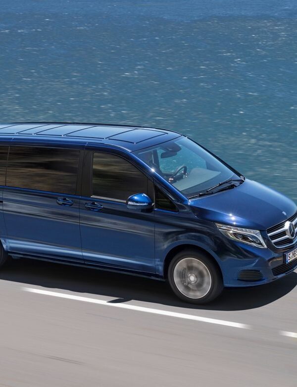 A Mercedes V-Class luxury van driving along a scenic road, surrounded by breathtaking views, symbolizing the comfort and exclusivity of a private tour experience.