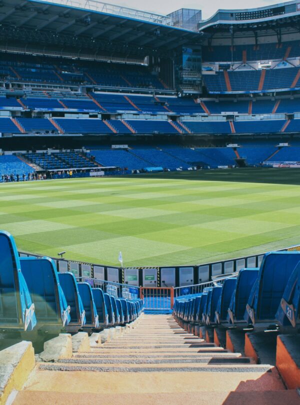 A panoramic view of a famous football stadium, with empty stands surrounding a vibrant green pitch and floodlights ready for an exciting match.